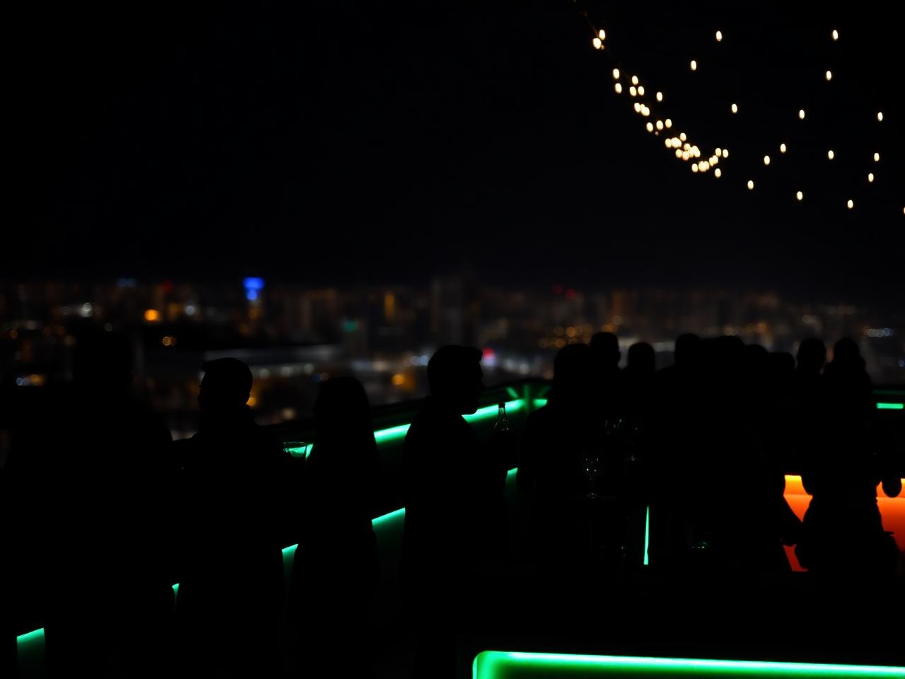 A rooftop bar at dusk with silhouetted professionals under string lights.